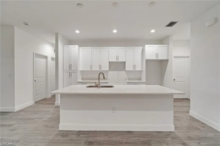 Kitchen featuring white cabinets, light wood-type flooring, a kitchen island with sink, and sink