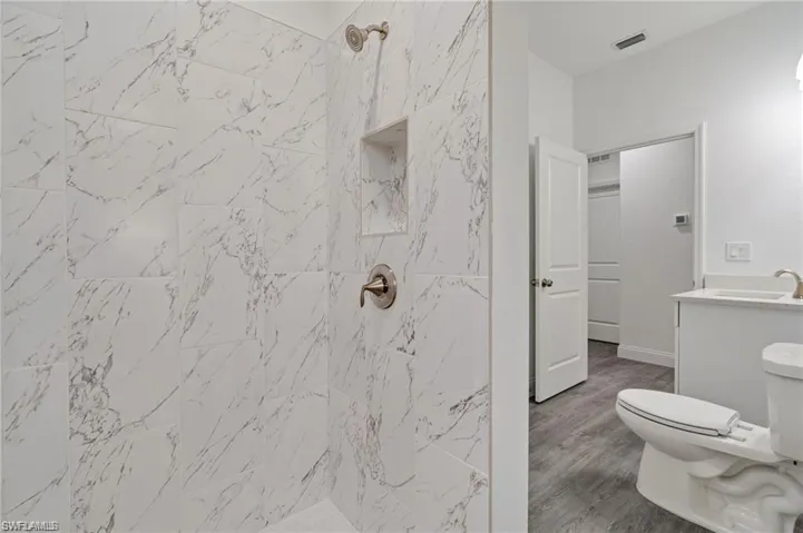 Bathroom with tiled shower, toilet, and hardwood / wood-style floors