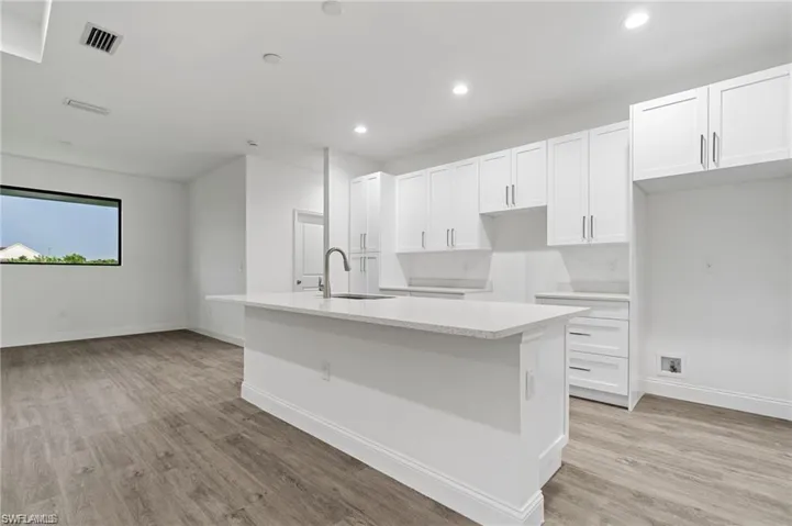 Kitchen with white cabinetry, sink, light wood-type flooring, and an island with sink