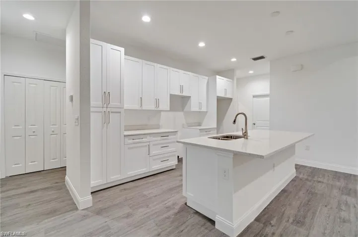 Kitchen featuring sink, white cabinets, light hardwood / wood-style floors, and an island with sink