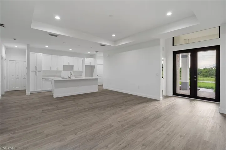 Unfurnished living room featuring sink, wood-type flooring, french doors, and a raised ceiling