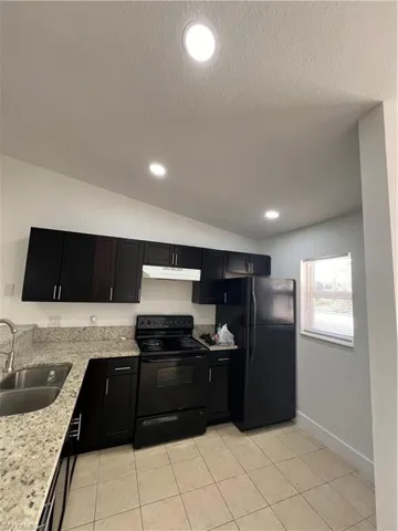 Kitchen featuring stove, fridge, extractor fan, a sink, and dark cabinetry