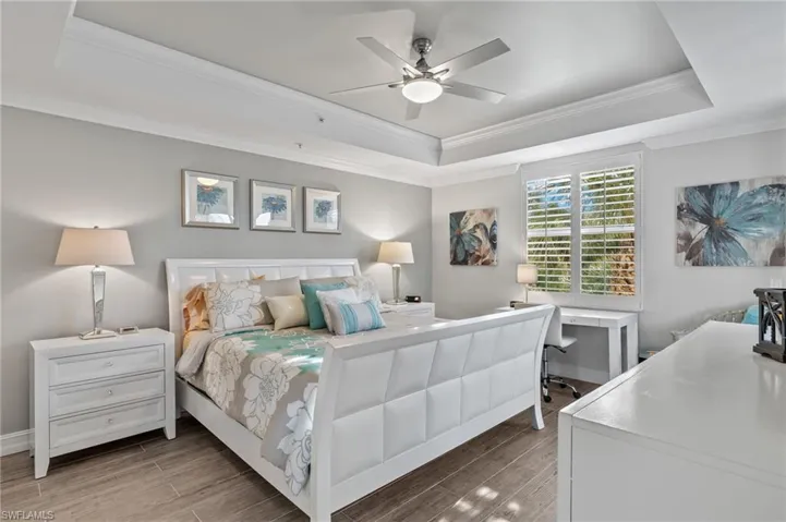 Primary bedroom with wood style tile floor, tray ceiling and ceiling fan.