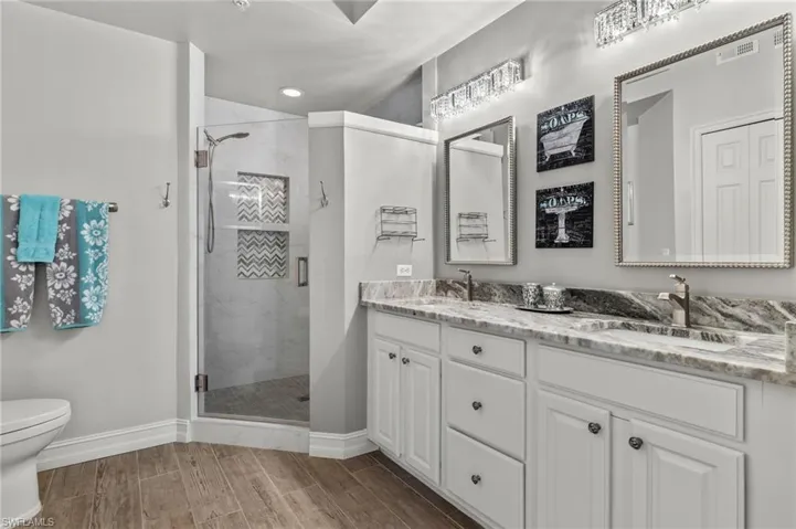 Updated primary bathroom offers granite counters, frameless glass shower door and custom lighting.