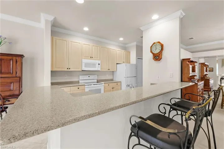 Kitchen featuring crown molding, light quartz counters, a peninsula, and white appliances