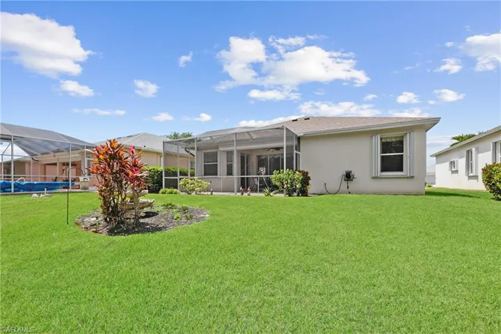 Rear view of property featuring screen enclosure, a lawn, and stucco siding