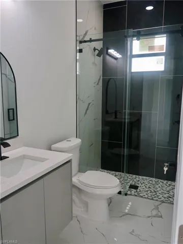 Full bath with vanity, marble look tiles, and a stall shower