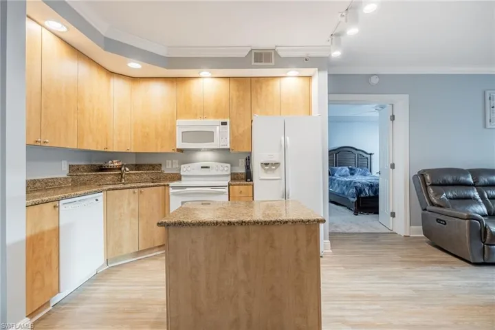 Kitchen featuring crown molding, dark stone countertops, white appliances, a center island, and light brown cabinets