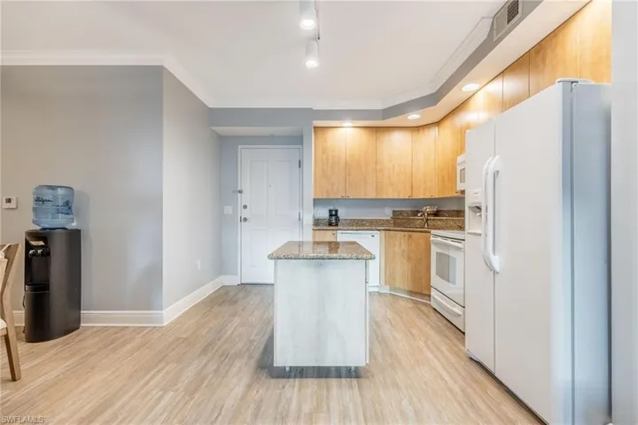 Kitchen with white appliances, light stone countertops, crown molding, a center island, and light brown cabinetry