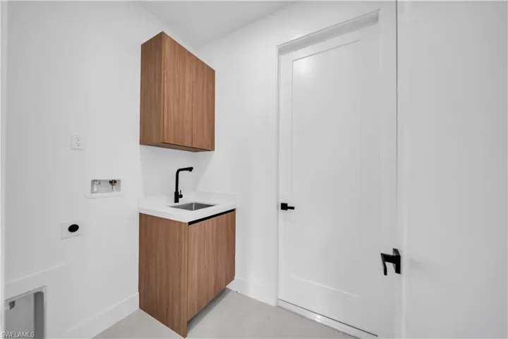 Laundry area featuring wood-finish cabinetry, a white countertop with an undermount sink, and a matte black faucet