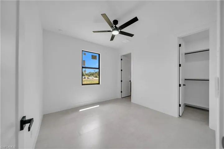 Bright interior space featuring a window with black trim, a contemporary black ceiling fan with integrated lighting, two doorways, and a closet with shelving and hanging rods