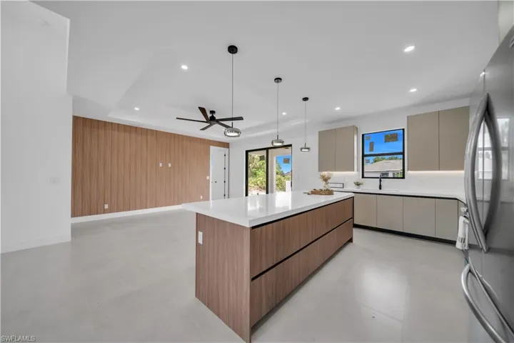 Modern kitchen featuring a large central island with a solid surface countertop, wood-finish cabinetry, and pendant lighting