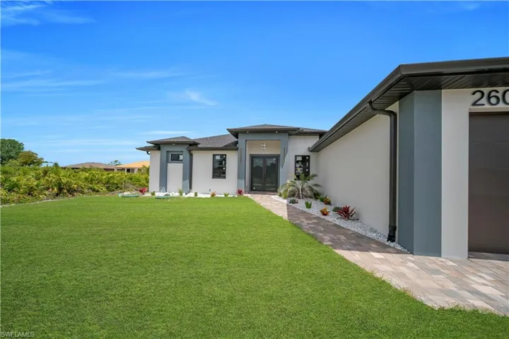 Contemporary exterior with a smooth stucco finish, dark gray accents, a paver driveway, and a coordinating paver walkway leading to the double-door entry