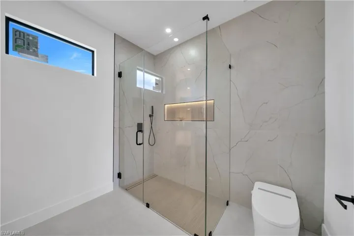 Walk-in glass shower enclosure with matte black hardware, integrated wall niche with accent lighting, and large format tile surround