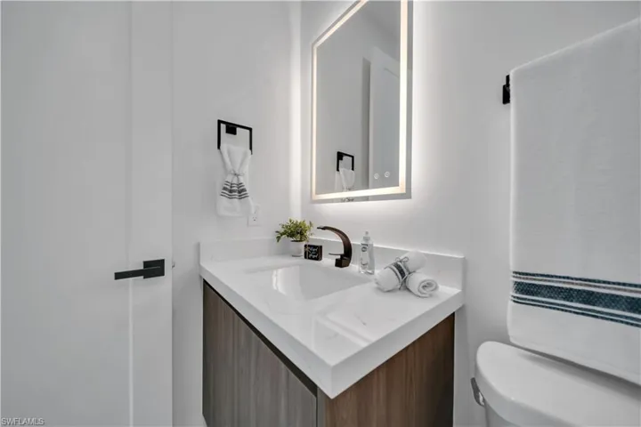 Modern vanity featuring a wood-finish cabinet, white countertop with integrated sink, and dark bronze faucet