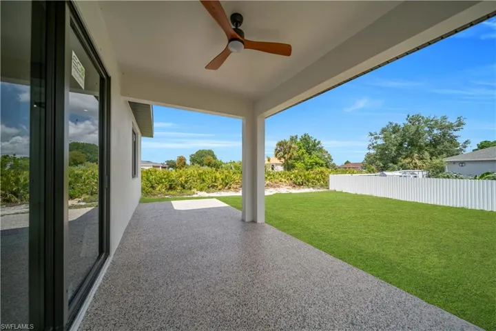 Expansive covered patio featuring a textured concrete surface, a ceiling fan with wood-finish blades, and a white support column
