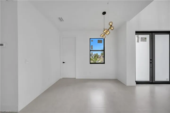Spacious room with light-colored flooring, a modern multi-bulb chandelier, a large window, a solid interior door with black hardware, and a double-door exterior entry