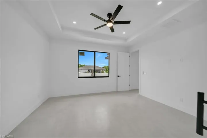 Spacious room featuring a tray ceiling with recessed lighting, a contemporary black ceiling fan, and large windows with black framing
