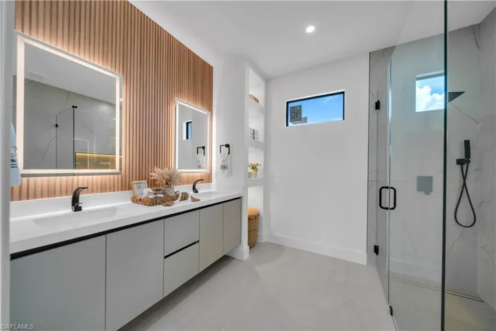 Contemporary bathroom featuring a double vanity with integrated sinks, matte black fixtures, and illuminated mirrors