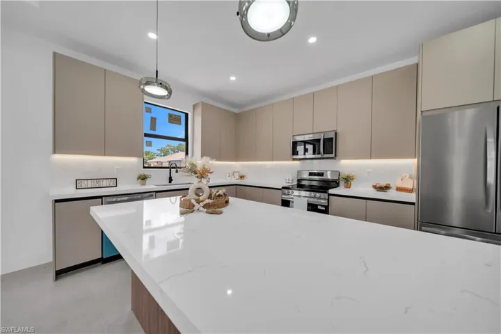 Kitchen featuring a large central island with a white countertop, flat-panel cabinetry, stainless steel appliances, and recessed lighting