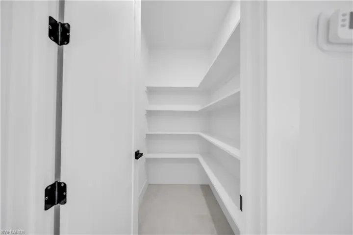 Walk-in pantry featuring built-in shelving, white walls, and light-toned flooring
