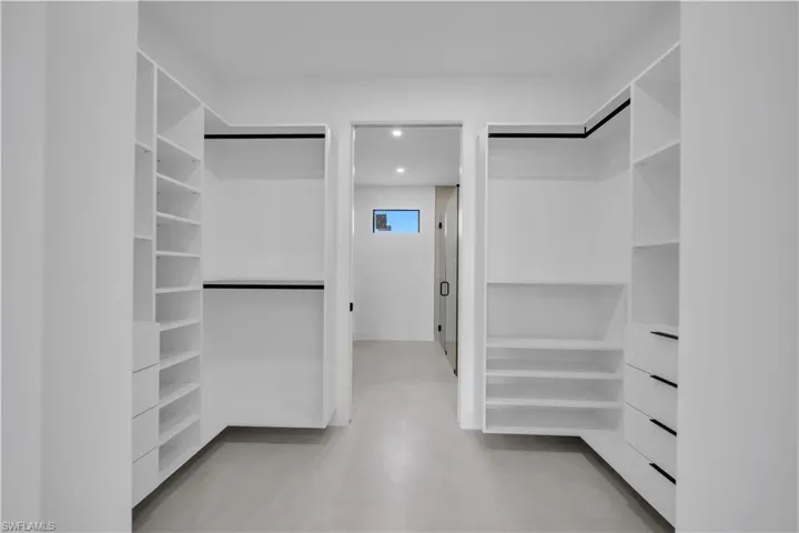 Spacious walk-in closet featuring extensive built-in shelving, multiple hanging rods, and integrated drawers