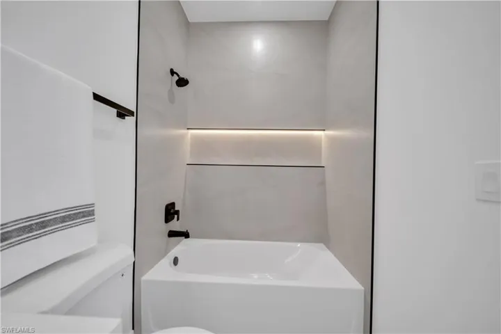 Contemporary bathtub and shower combination featuring large format tile surround, matte black shower fixtures, an illuminated recessed niche, and a contrasting black trim accent