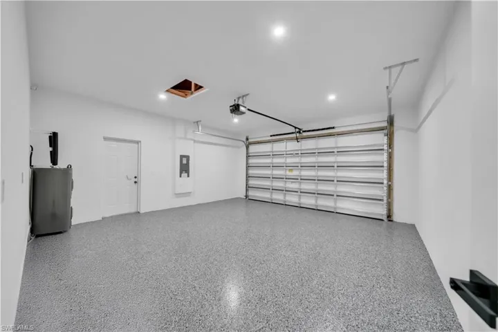 Spacious garage featuring epoxy flooring, overhead door with automatic opener, recessed lighting, and white walls