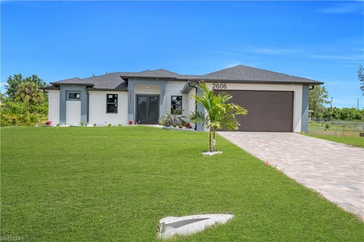 Modern single-story residence featuring a dark asphalt shingle roof, a two-car garage with a brown door, and a paver driveway