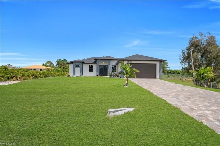 Modern single-story residence with a paver driveway, two-car garage, and a lush green lawn