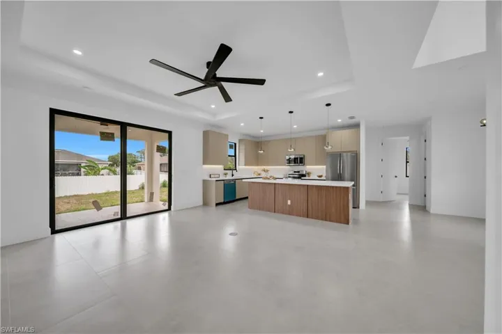 Spacious interior featuring light-toned tile flooring, recessed lighting, and a modern kitchen with a large island and stainless steel appliances