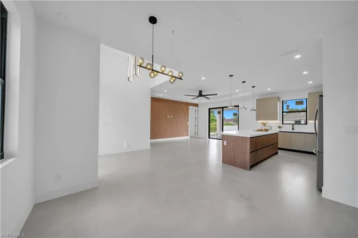 Open-concept interior featuring light gray tile flooring, a modern linear chandelier, and a wood-paneled accent wall