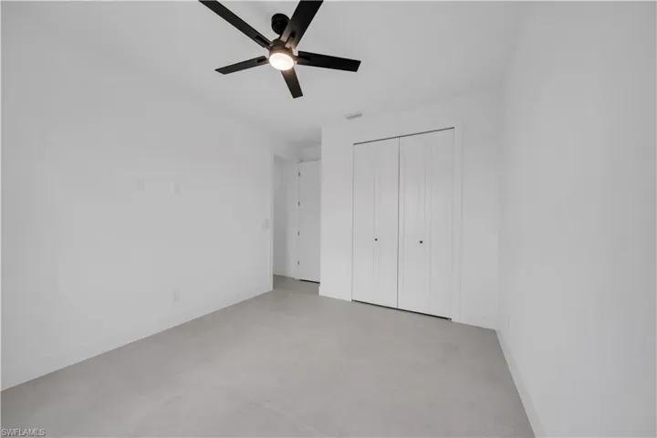 Light-filled room featuring a ceiling fan with integrated lighting, a spacious bi-fold closet, clean white walls, and contemporary gray tile flooring