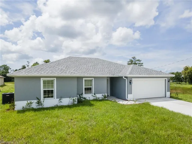 Ranch-style house with an attached garage, roof with shingles, stucco siding, driveway, and a front lawn
