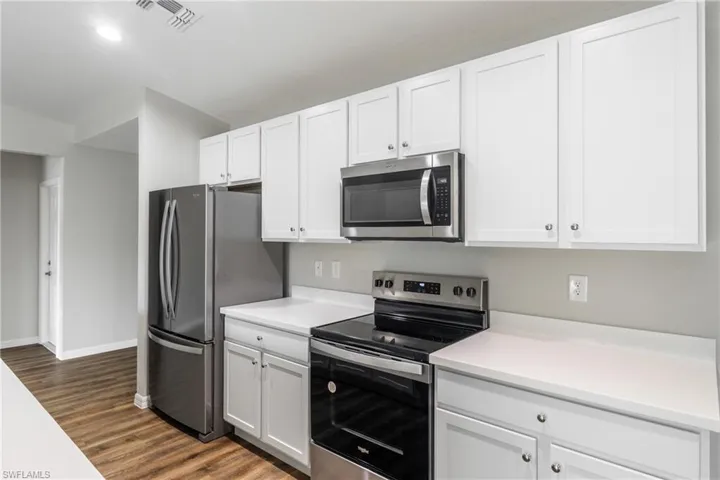 Kitchen with appliances with stainless steel finishes, white cabinetry, dark wood-type flooring, light countertops, and recessed lighting
