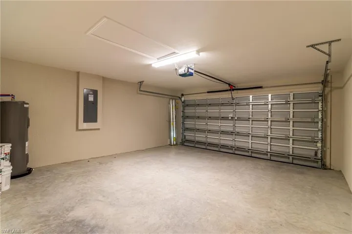 Garage with electric water heater, electric panel, and a garage door opener