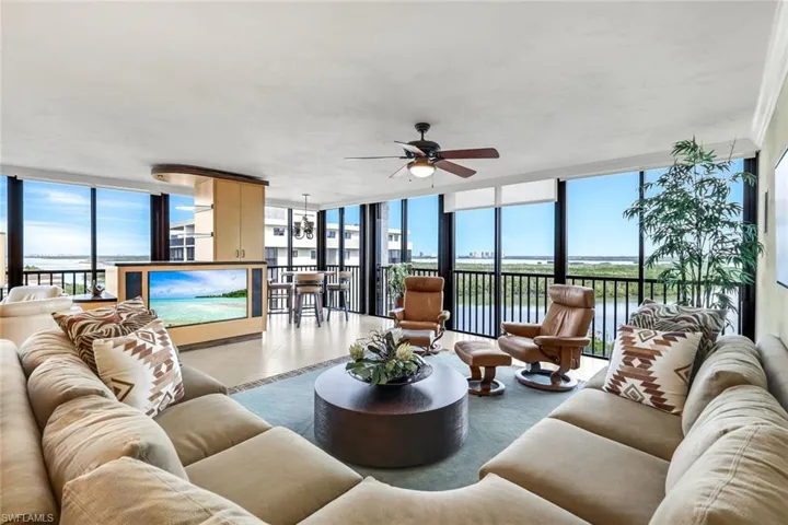 Tiled living room featuring expansive windows, a ceiling fan, a water view, and a chandelier