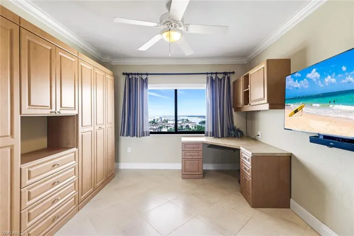Unfurnished office with built in desk, crown molding, a ceiling fan, and light tile patterned flooring