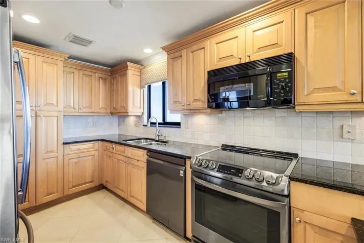 Kitchen with appliances with stainless steel finishes, tasteful backsplash, dark stone counters, light tile patterned floors, and recessed lighting