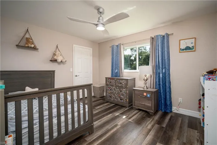 Bedroom with ceiling fan, dark hardwood / wood-style flooring, and a crib