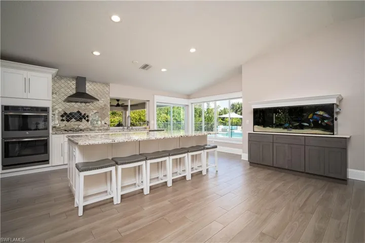 Kitchen with stainless steel double oven, white cabinetry, a kitchen island, and wall chimney range hood