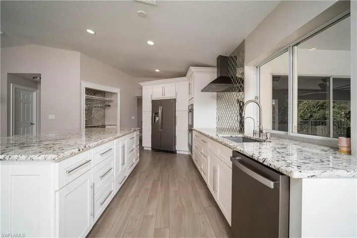 Kitchen with sink, wall chimney exhaust hood, stainless steel appliances, light hardwood / wood-style flooring, and white cabinets