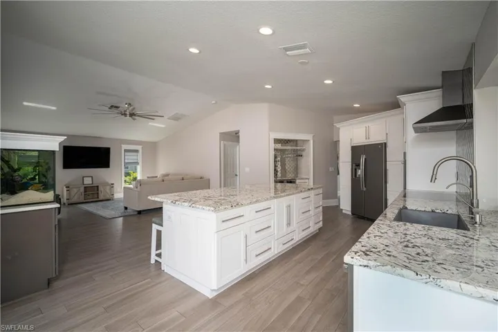 Kitchen featuring wall chimney exhaust hood, sink, white cabinets, and stainless steel refrigerator with ice dispenser