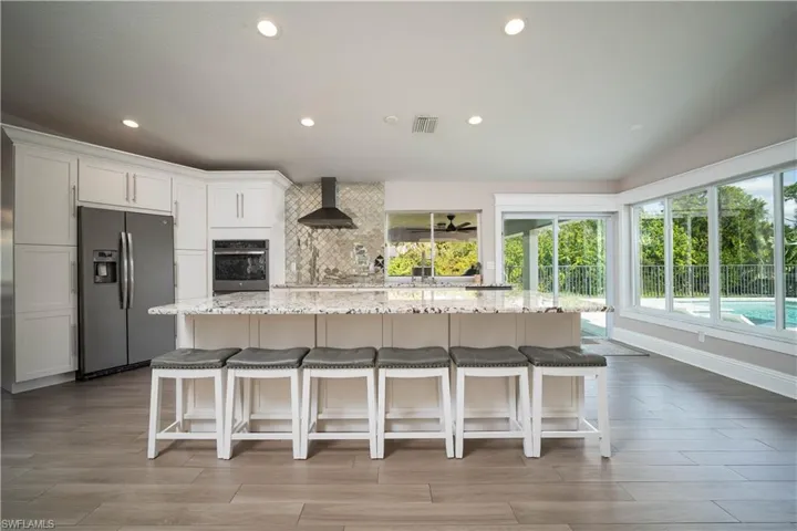 Kitchen featuring plenty of natural light, white cabinets, wall chimney range hood, and appliances with stainless steel finishes