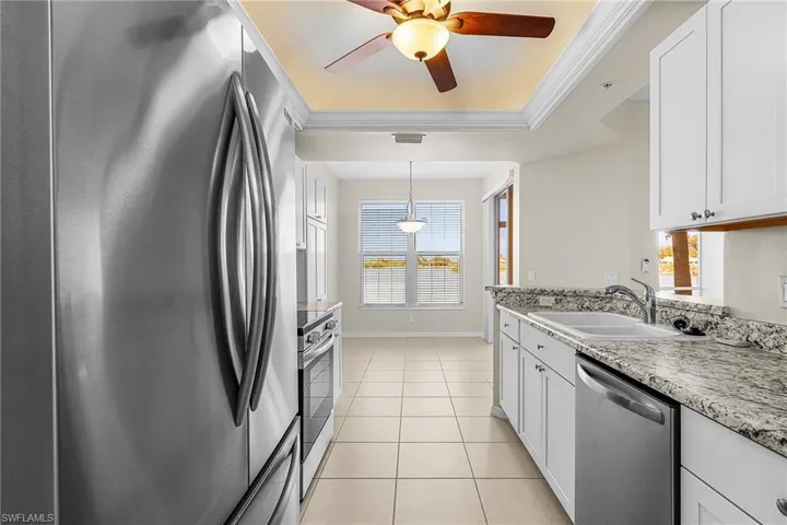Kitchen with stainless steel appliances, ornamental molding, white cabinetry, light tile patterned floors, and a ceiling fan