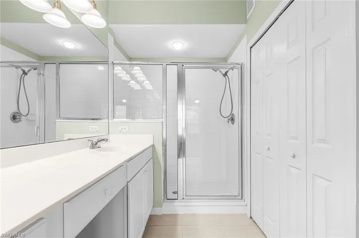 Bathroom with a closet, vanity, a shower stall, and light tile patterned floors