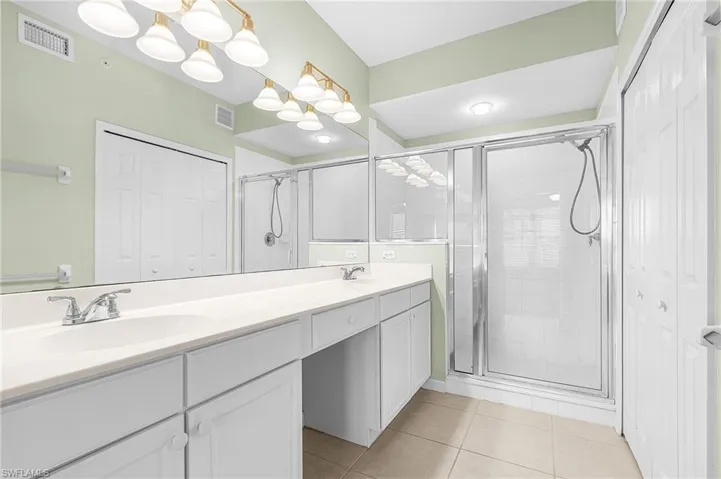Bathroom with a closet, double vanity, a shower stall, and light tile patterned floors