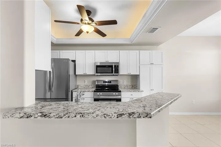Kitchen featuring stainless steel appliances, ornamental molding, white cabinetry, a ceiling fan, and a peninsula