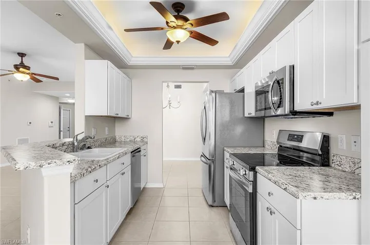 Kitchen with a ceiling fan, stainless steel appliances, ornamental molding, white cabinetry, and a tray ceiling