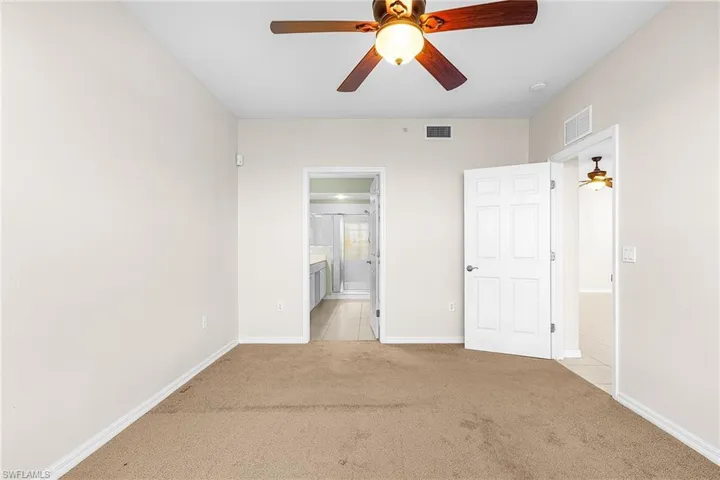 Unfurnished bedroom featuring light carpet, ceiling fan, and ensuite bathroom